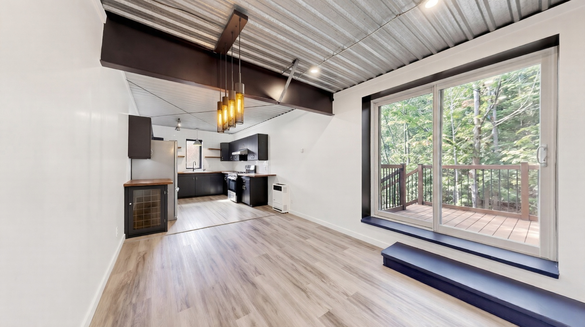 Living space with exposed steel beam and a wall of glass overlooking the forest