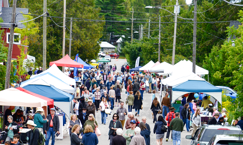 Crowds gathering at the Eden Mills Writers' Festival along the riverside street, with white reading tents and vendors